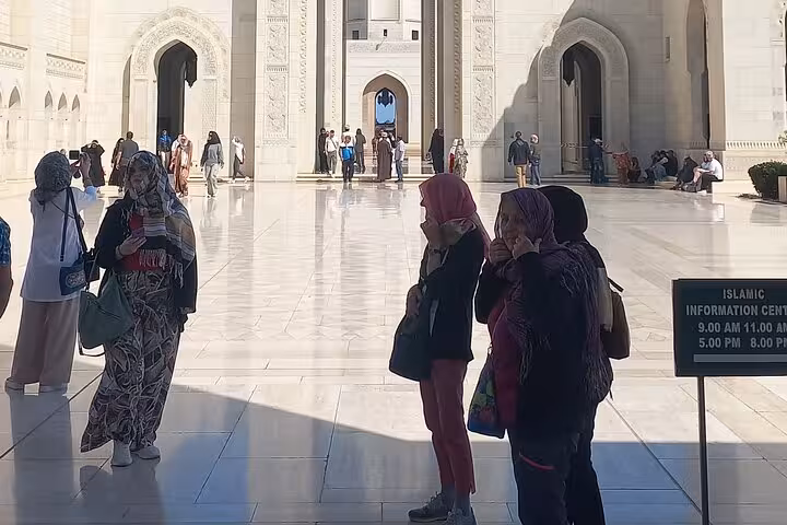 Tourists in headscarves walk across the gleaming courtyard of Sultan Qaboos Grand Mosque on a Muscat city tour
