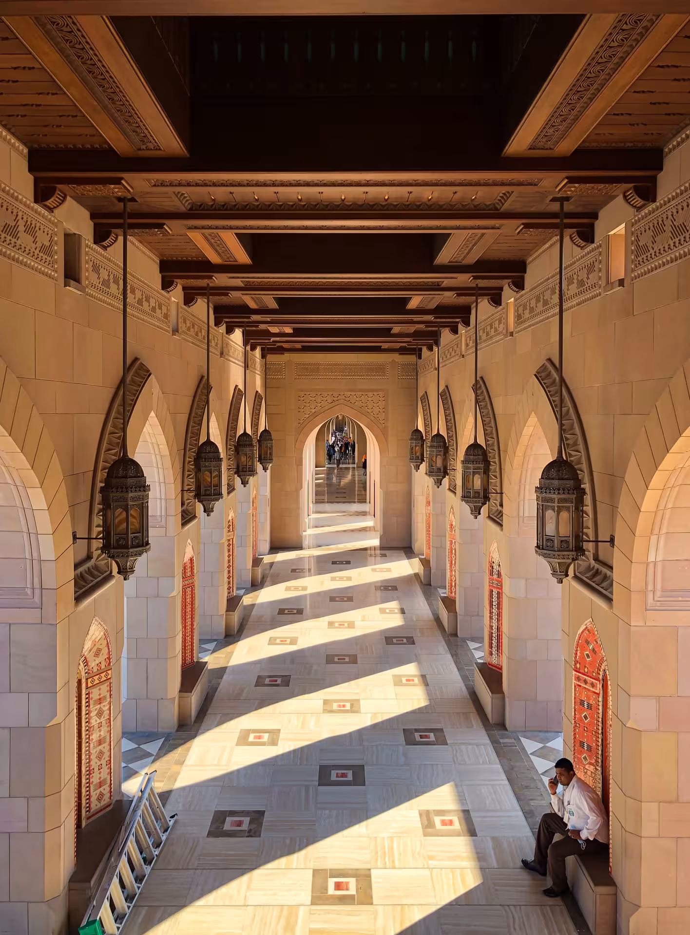 Sunlit colonnade with ornate lanterns and arches at Sultan Qaboos Grand Mosque on a private half-day Muscat city tour
