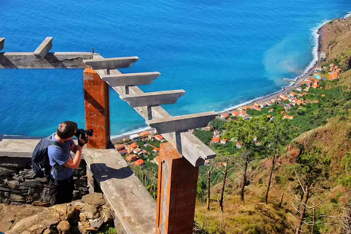 Photographer capturing stunning coastal views from a scenic overlook, featuring vibrant blue waters and a charming village below.
