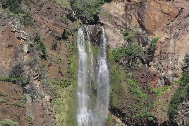 Scenic waterfall cascading down rocky cliffs, surrounded by lush greenery, featured in Sunny Southwest tour with rum and lighthouse exploration.