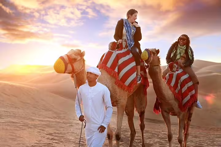 Travelers on camel ride with guide at sunrise in Dubai desert, enjoying private safari experience.