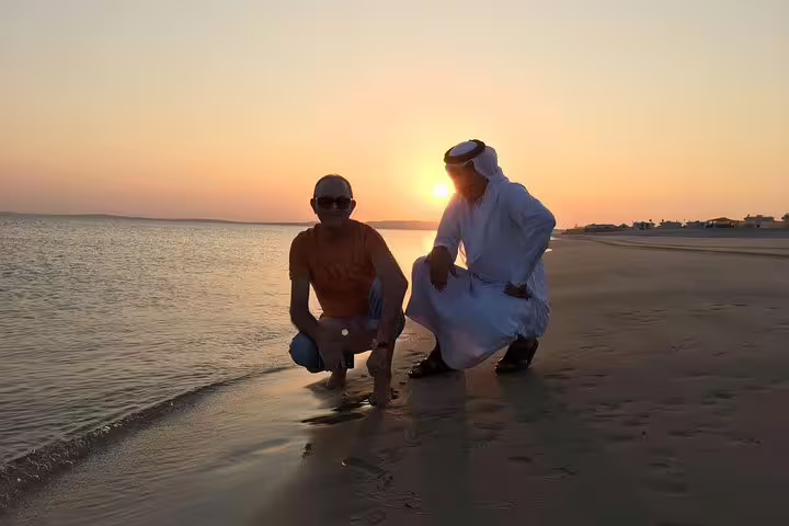 Two men enjoying a serene sunrise at a beach in Qatar, perfect for a desert safari experience.