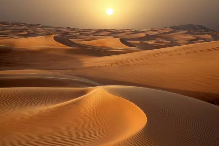 Golden sunrise illuminating Dubai's expansive desert dunes, ideal for a tranquil safari adventure.