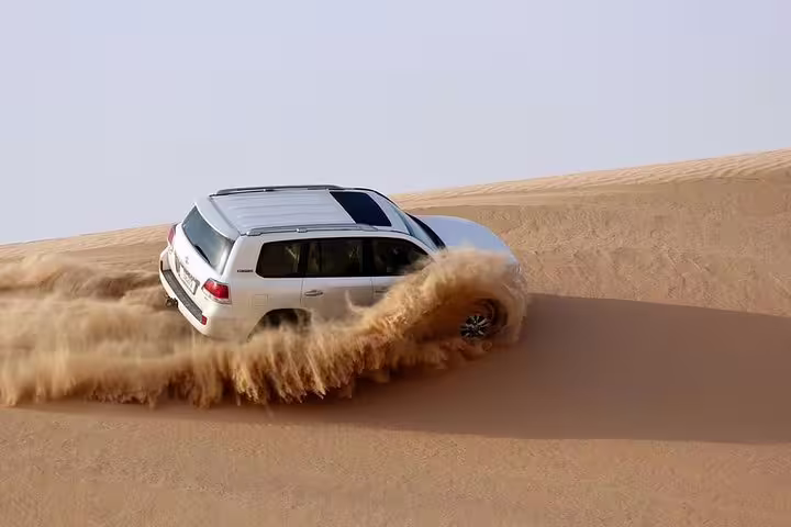 Off-road vehicle navigating golden sand dunes during a thrilling sunrise desert safari in Qatar.