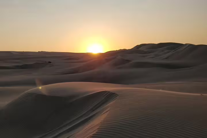 Serene sunrise casting golden hues over the vast desert landscape in Qatar, highlighting dune contours.