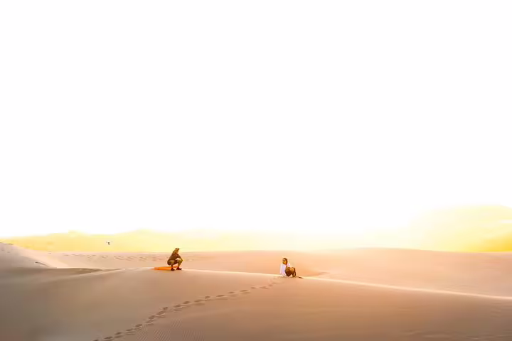 Two people enjoy the serene beauty of a sunrise over the vast sand dunes during a desert safari in Qatar.