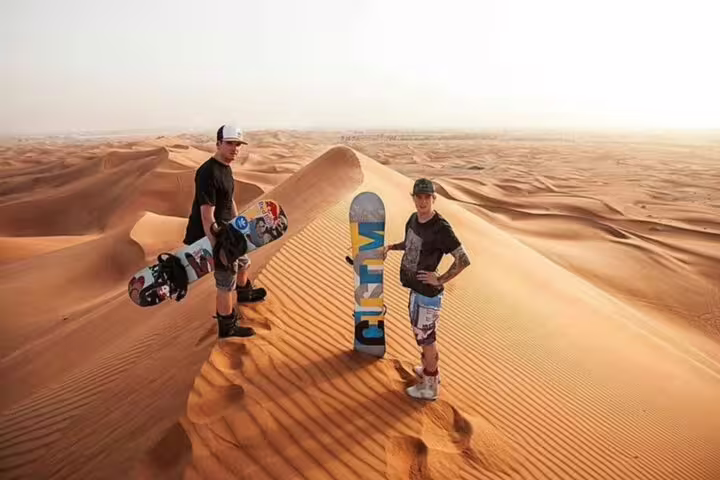 Adventurers sandboarding on vast Dubai desert dunes during a sunrise safari experience.