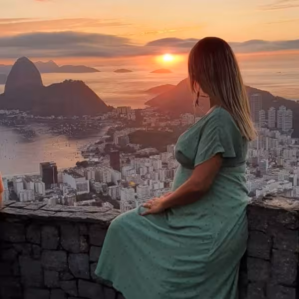 Woman in green dress watches serene sunrise over Rio de Janeiro's iconic Sugarloaf Mountain from Dona Marta Viewpoint.