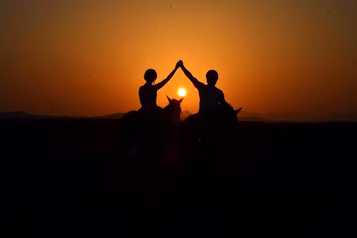 Silhouetted riders high-five at sunrise on Marsa Alam desert horseback tour, scenic beach and dunes ride