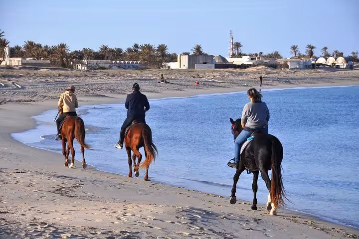 Riders trekking along Marsa Alam Red Sea beach on horseback, coastal desert scenery on 3-hour sunrise tour