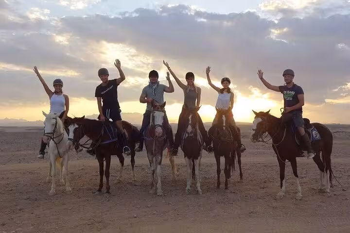 Group sunrise horse riding in Marsa Alam desert, riders waving on horseback during 3-hour beach and desert tour