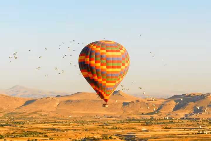 Sunrise hot air balloon ride over desert valleys, colorful balloon floating above golden landscape and hills
