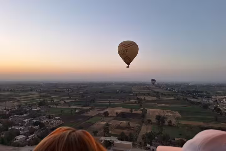 Hot air balloon glides over lush fields of Luxor West Bank at sunrise, capturing the serene beauty of Egypt from above.