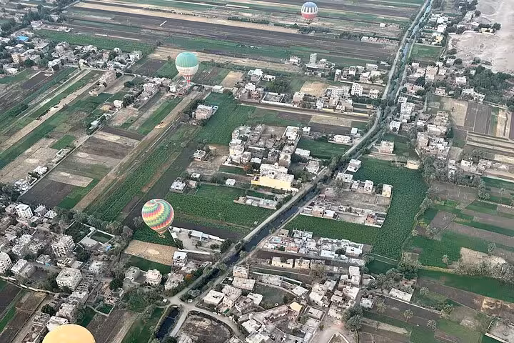 Aerial view of hot air balloons floating over Luxor's lush fields and villages at sunrise.