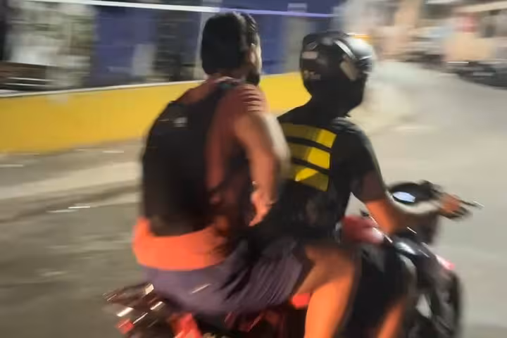 Two people riding a motorcycle on a bustling street during the Sunrise Walk Two Brothers tour.