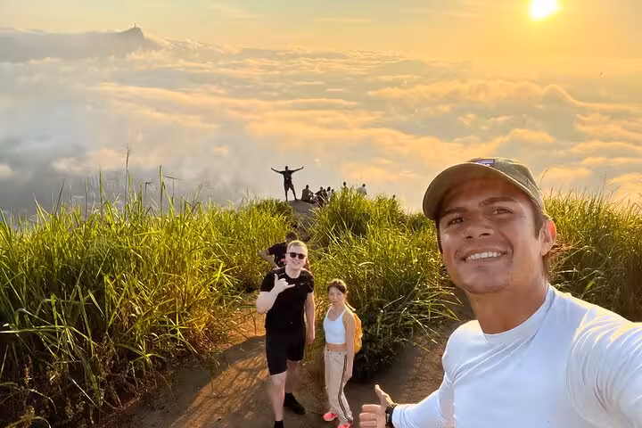 Group enjoying sunrise atop Two Brothers Mountain with stunning cloudscape and sunlit horizon in the background.
