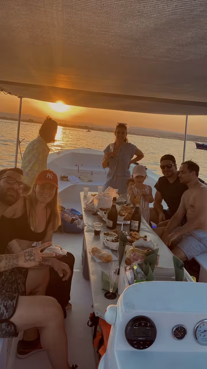 Group enjoying a lively sunset aperitif on a boat, featuring drinks and snacks during the tour.