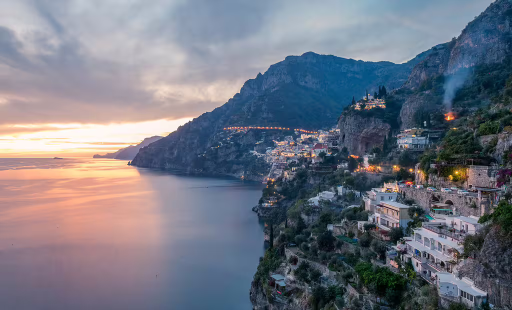 Sunset boat tour view of Positano cliffs and Amalfi Coast villages glowing above calm Tyrrhenian Sea waters near Sorrento