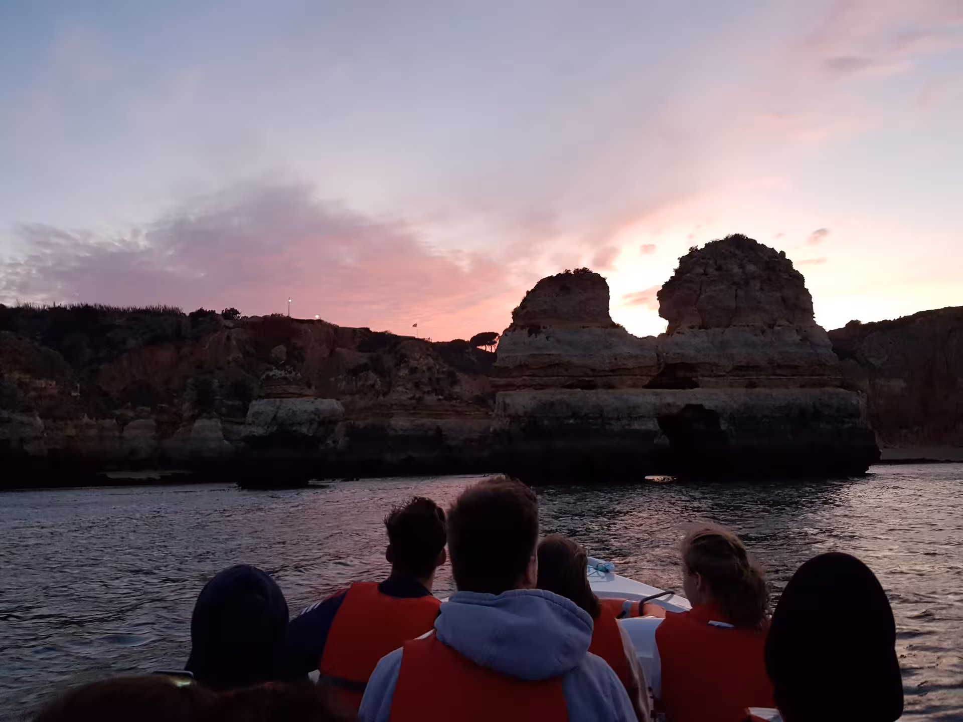 Tourists on a sunset boat tour at Ponta da Piedade, Lagos admiring rugged Algarve cliffs glowing under pink and purple skies