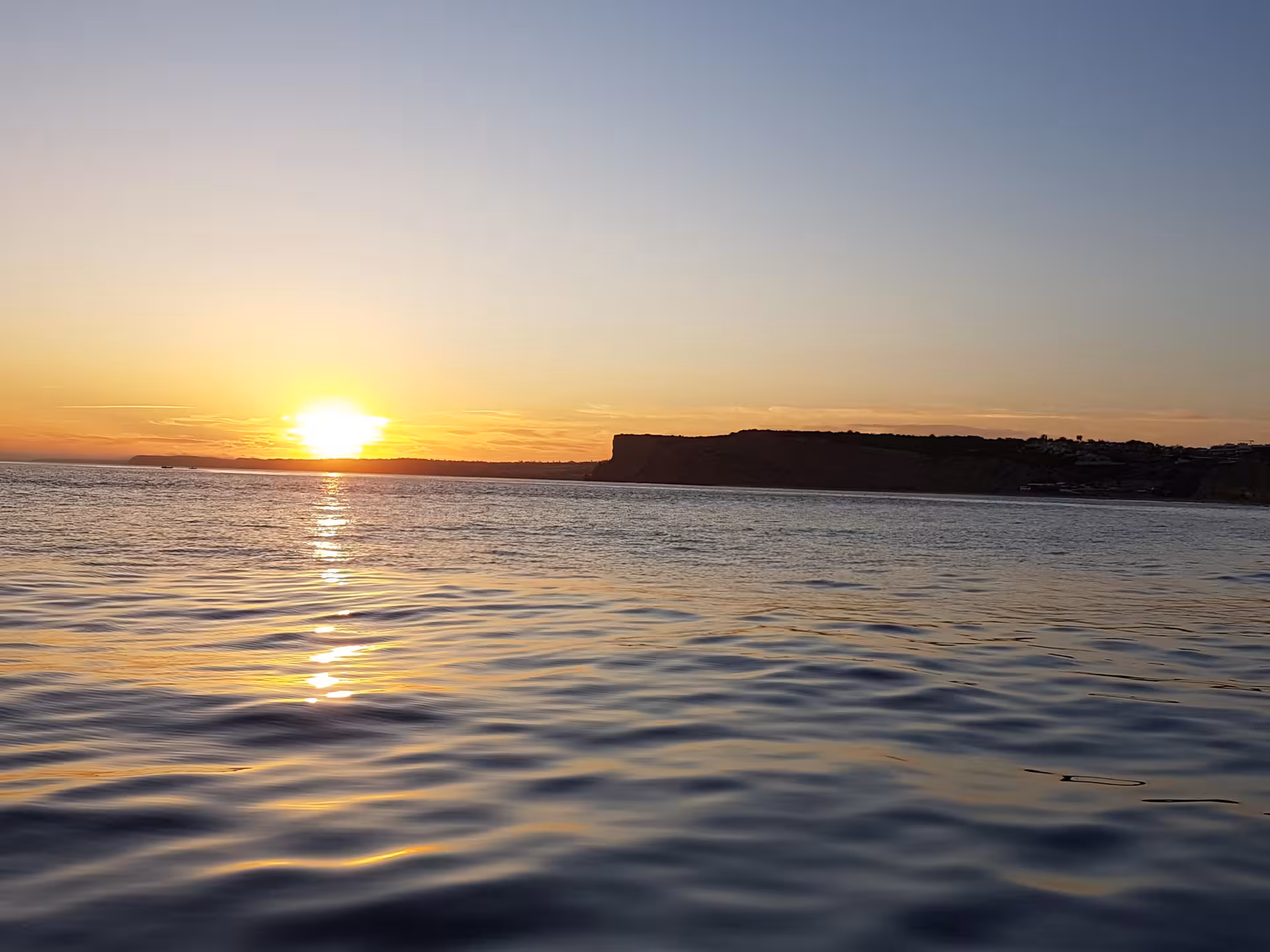 Calm Atlantic waters reflect a vivid golden sunset near the cliffs of Ponta da Piedade during a Lagos Algarve boat tour