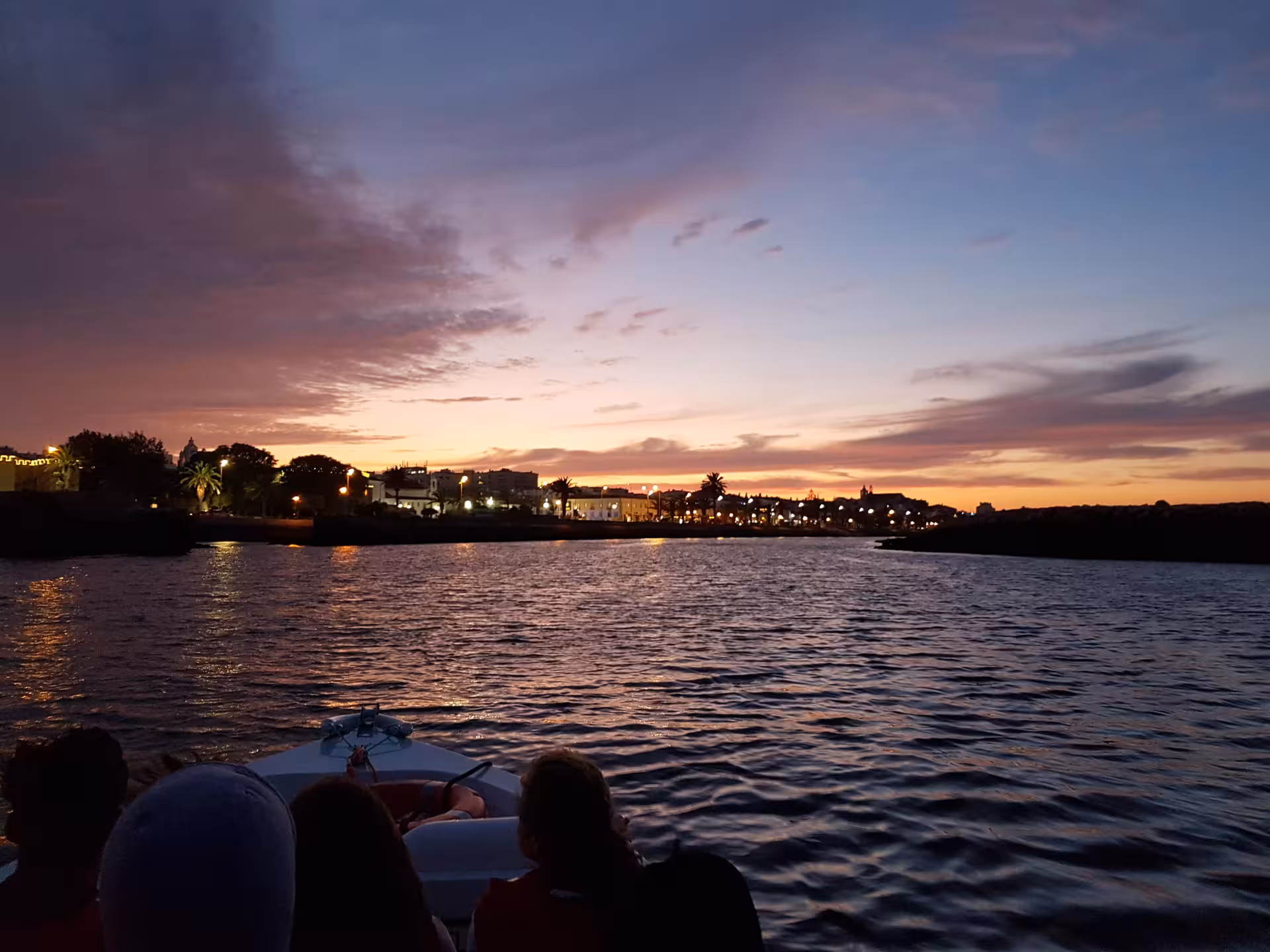 Tourists relax on a sunset boat cruise from Lagos, watching colorful skies and waterfront lights along the Algarve coast