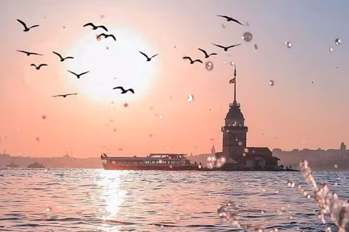 Sunset Bosphorus cruise passing Maiden’s Tower in Istanbul, seagulls flying over shimmering sea