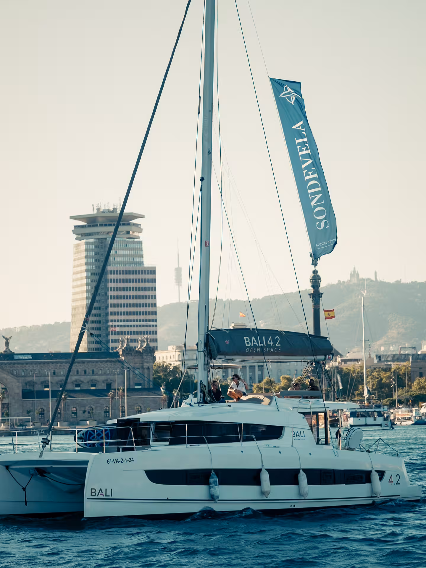 Sailing catamaran cruising Barcelona harbor at golden hour, perfect for a sunset catamaran tour on the Med