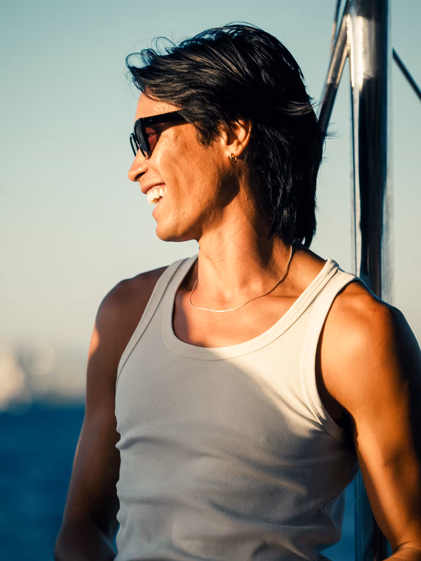Smiling guest in sunglasses enjoying golden hour breeze on a sunset catamaran cruise at sea