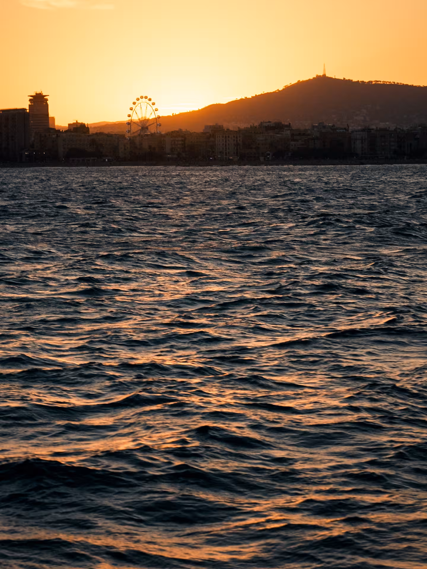 Sunset view from a catamaran with shimmering waves and coastal skyline, perfect evening sailing tour