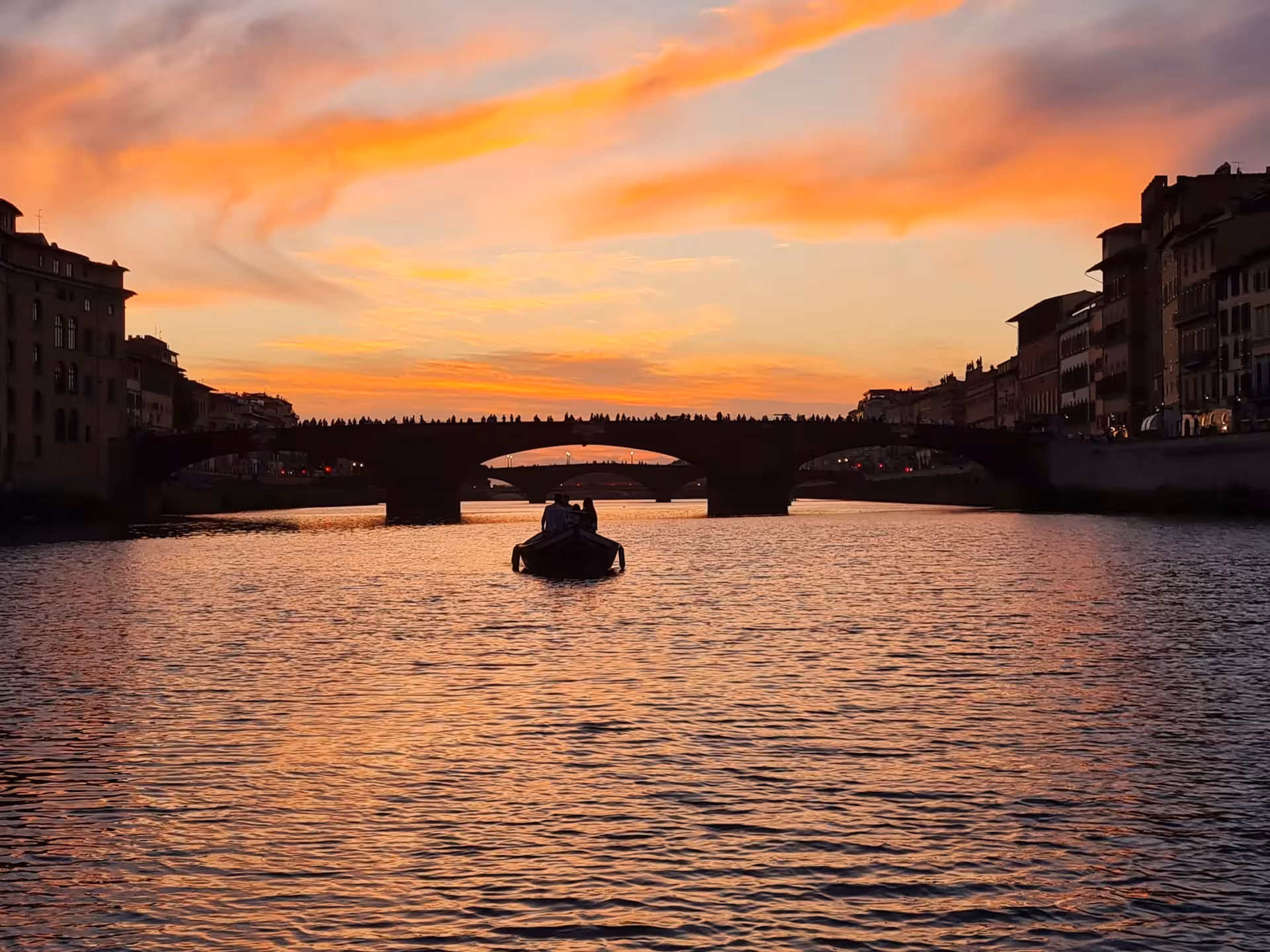 Breathtaking sunset over the Arno River with a boat silhouetted against the vivid sky.