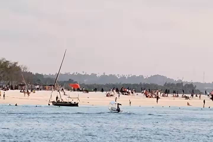 Visitors enjoy a vibrant beach scene with traditional dhows in Nungwi, Zanzibar, perfect for a sunset cruise experience.
