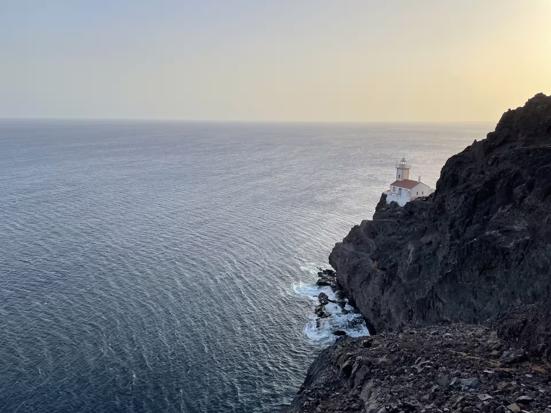 Dramatic coastal view of Lighthouse Dona Amélia perched on rugged cliffs during a serene sunset hike on the Atlantic Ocean.