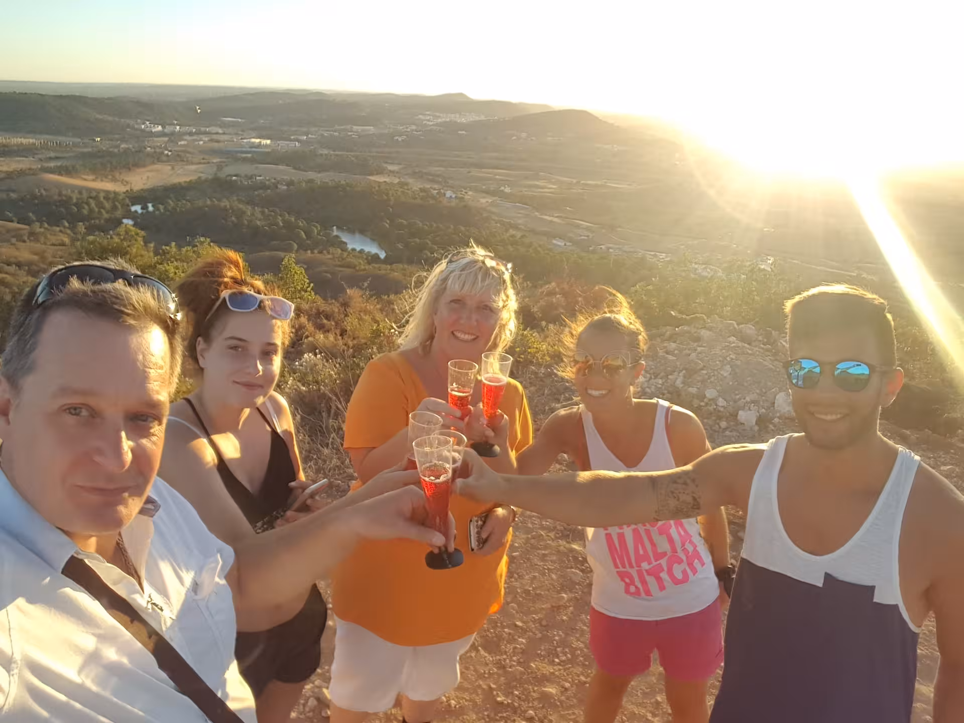 Group raising glasses of sparkling wine at a golden Algarve sunset viewpoint during a scenic jeep safari and dinner tour