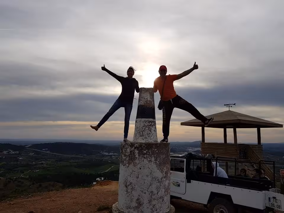 Sunset jeep safari in Algarve with two friends posing on a hilltop viewpoint pillar above rolling countryside and 4x4.