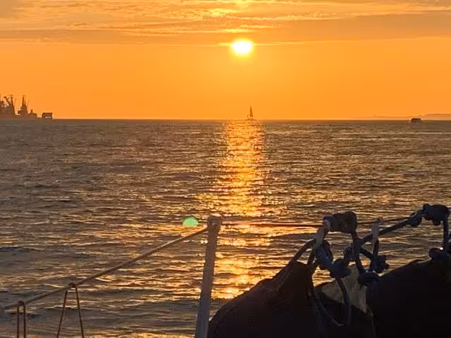 Sunset Lisbon Tour private cruise on the Tagus River with glowing horizon, sailboat silhouette and calm seas