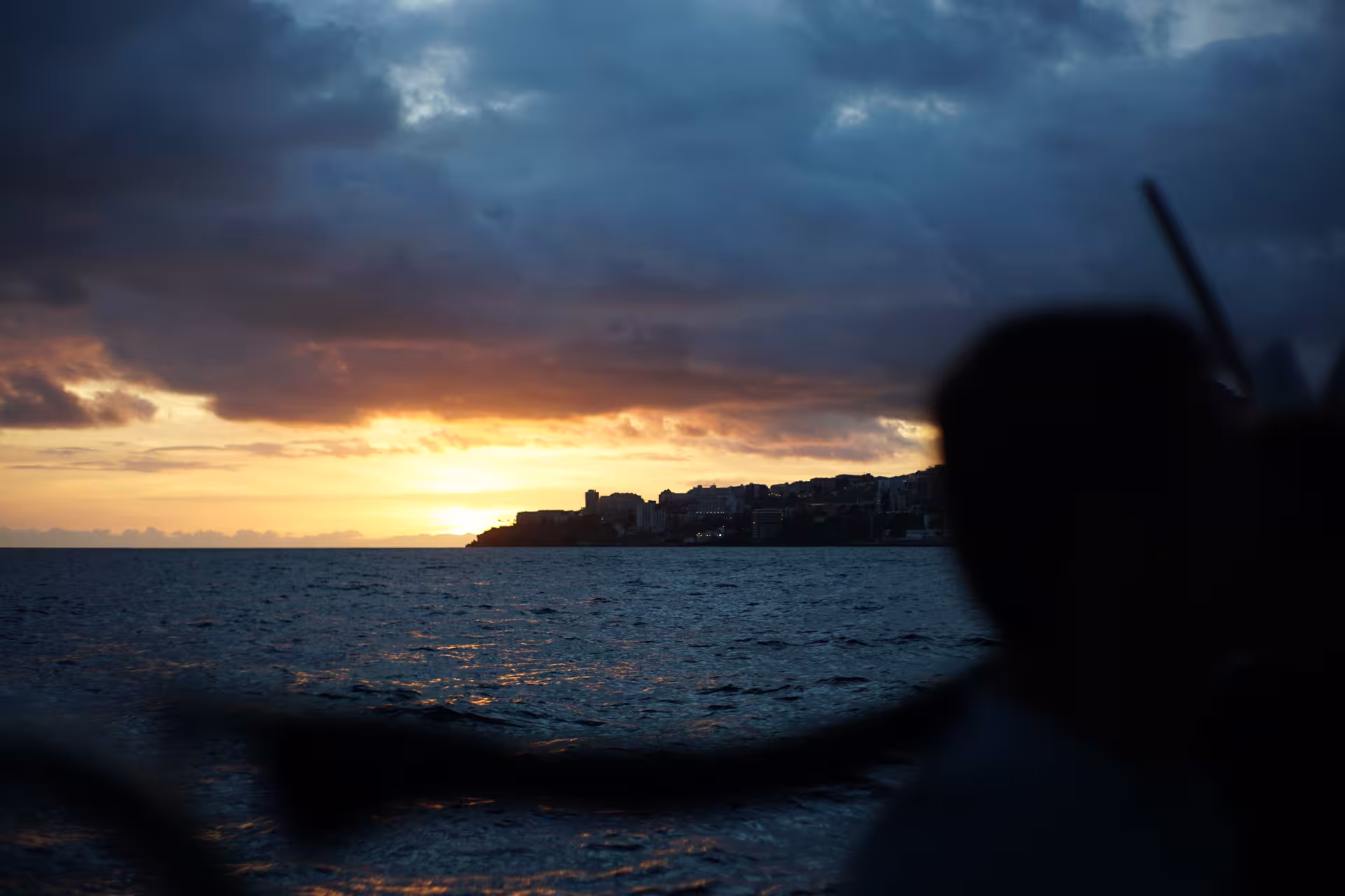 Dramatic sunset over ocean with silhouetted RIB boat, perfect for dolphin and whale watching tours.