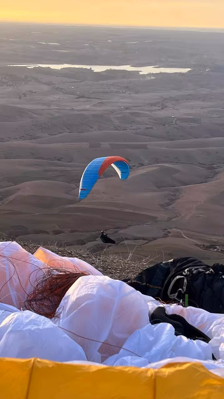 Paraglider soaring over Agafay Desert at sunset with scenic views near Marrakech, Morocco.