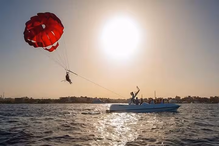 Sunset parasailing in Hurghada on the Red Sea, red parachute towed by speedboat with private transfer