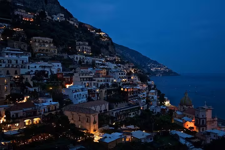 Twilight view of Positano's charming hillside homes illuminated along the Amalfi Coast, perfect for a sunset tour from Naples.