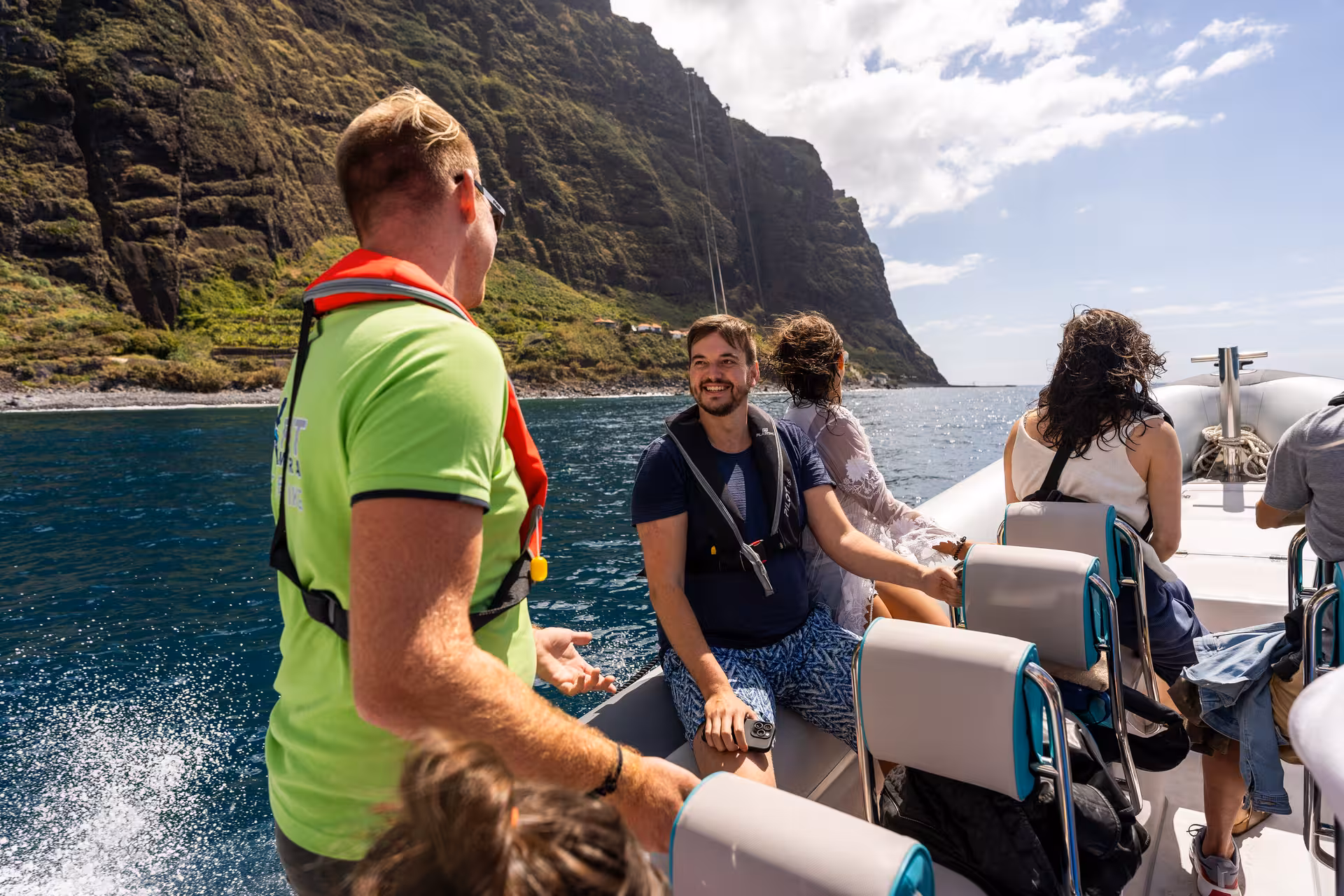 Happy tourists enjoying a scenic RIB boat ride along rugged cliffs on a sunny day.
