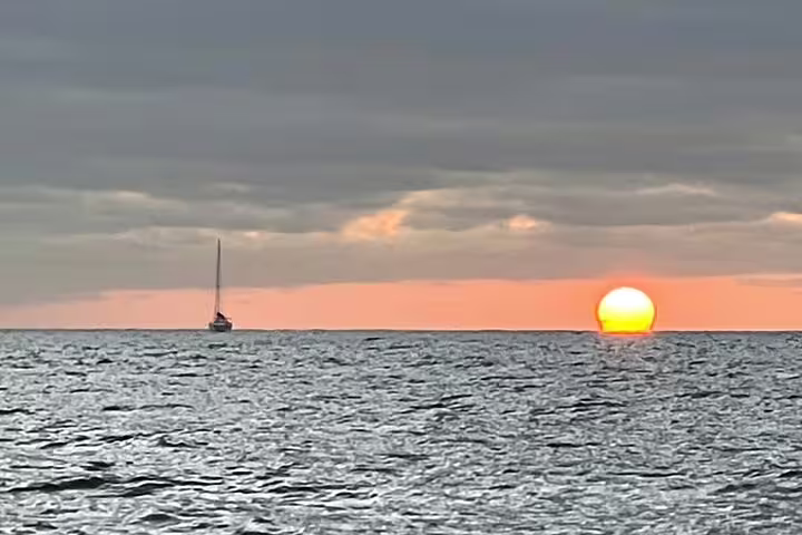 A serene sailing cruise in Madeira at sunset, with a sailboat silhouetted against a vibrant orange horizon over the ocean.