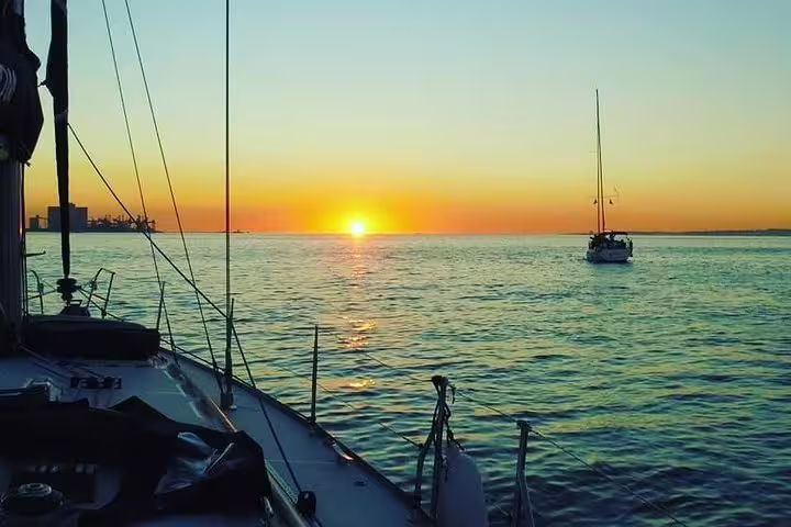 Serene sunset sailing on the Tagus River with boats silhouetted against the vibrant orange and blue horizon.