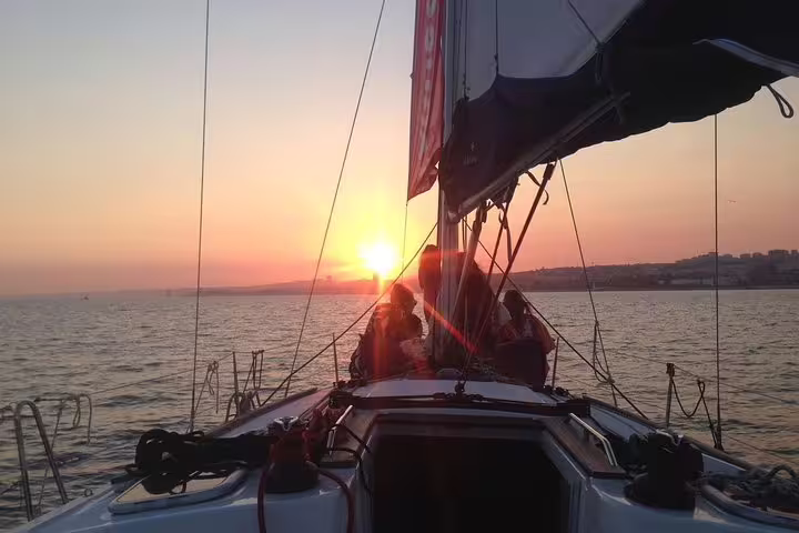Sailing at sunset on the Tagus River with a glowing horizon and Lisbon skyline in the background.