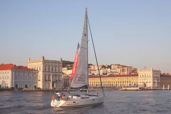 Sailboat cruising on the Tagus River at sunset with Lisbon's historic architecture in the background.