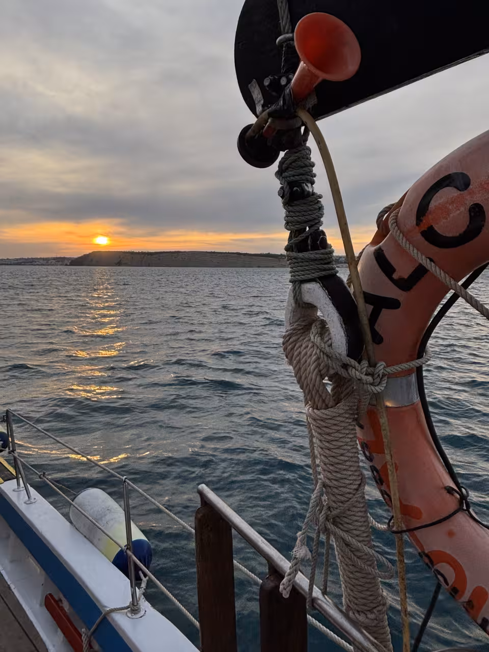 View from sailboat deck at dusk with lifebuoy and ropes, cruising toward sunset on a guided sunset sailing tour