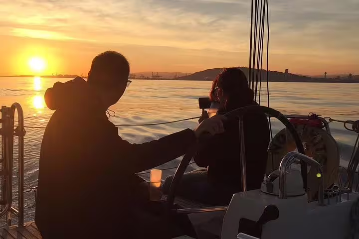 People enjoying a sunset sailing trip with drinks and snacks on a calm sea, perfect for a relaxing swim adventure.