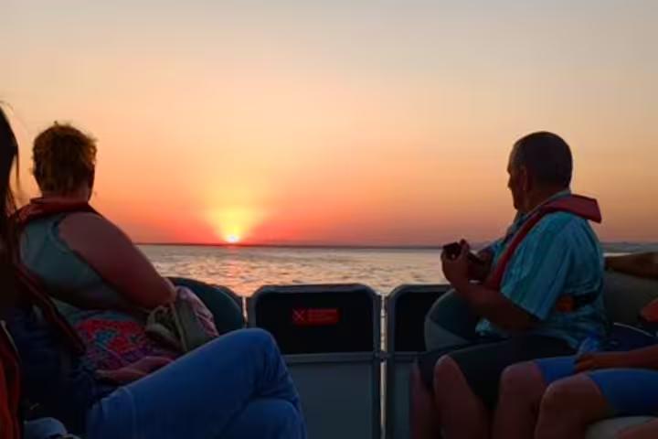 Guests relax on a boat deck watching a vivid ocean sunset during the Sunset Tour, perfect for evening sightseeing.