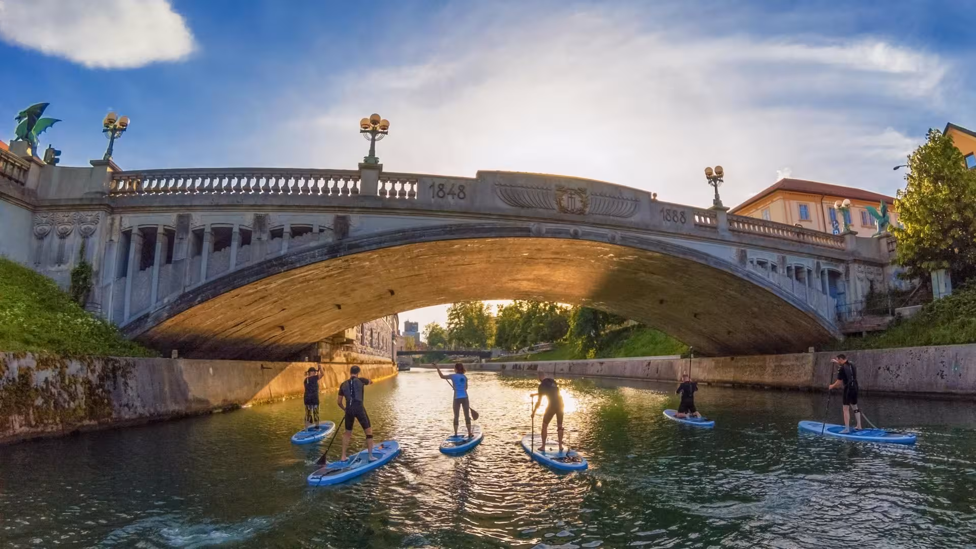 SUP Ljubljana sunset paddle under historic stone bridge on the Ljubljanica River, guided city tour experience