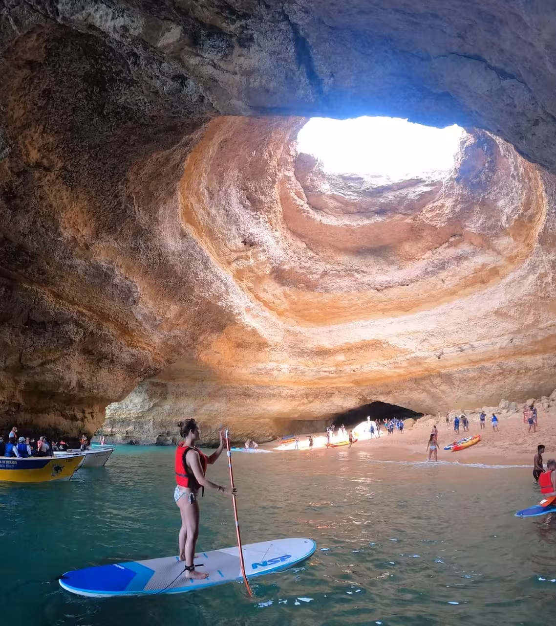 Paddleboarder explores a stunning sea cave with a natural skylight, offering a unique coastal adventure experience.