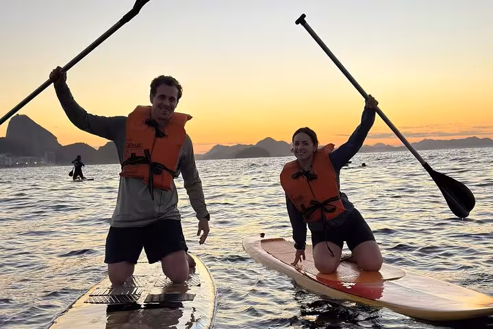 Two people paddleboarding at sunrise in Copacabana, capturing adventure and scenic views of the river.